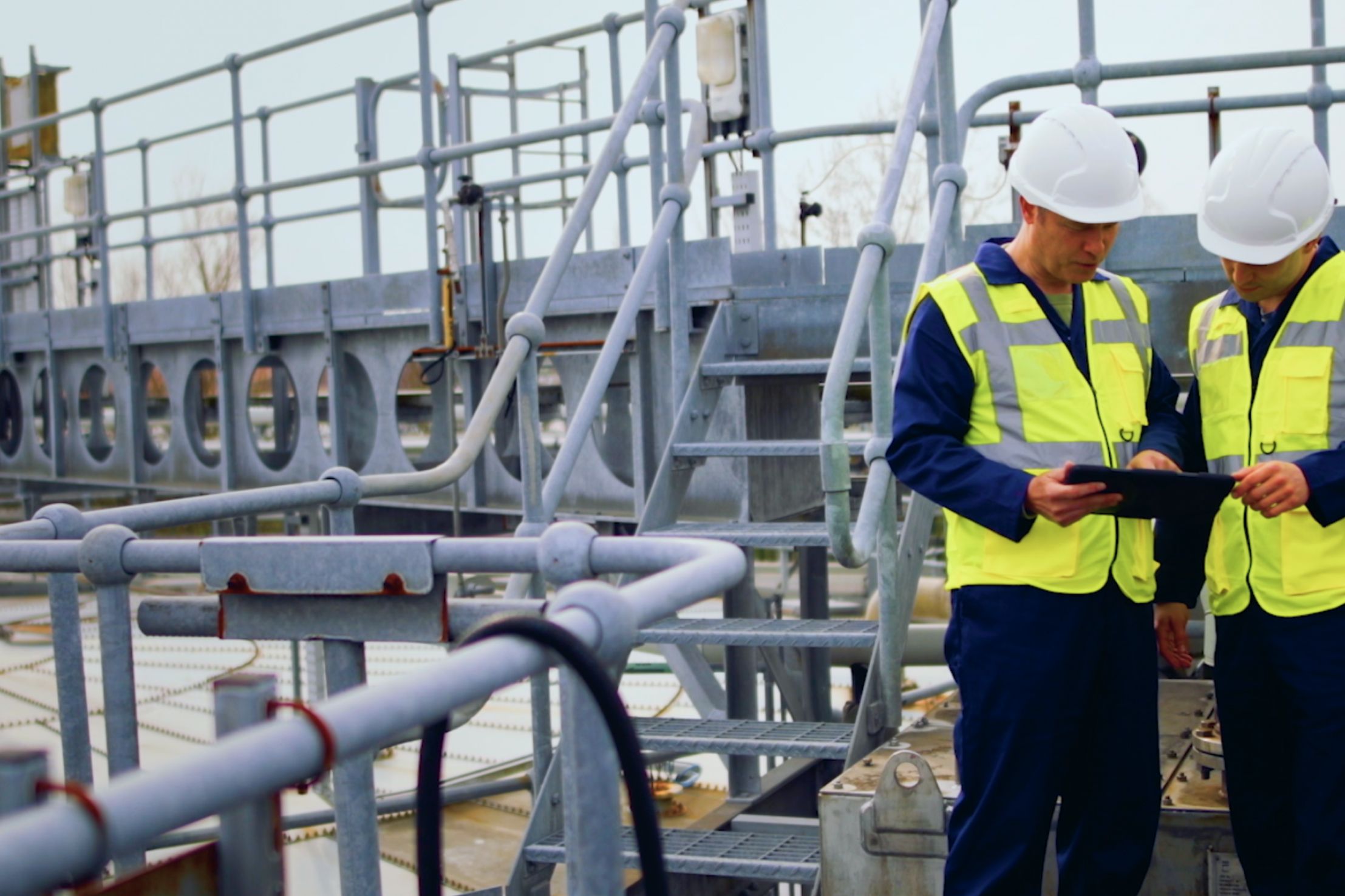 Two men with hardhat and reflective vests looking at tabelt on job site