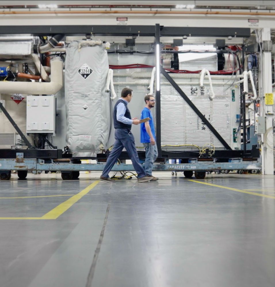 two men walking inside building next to large machinery