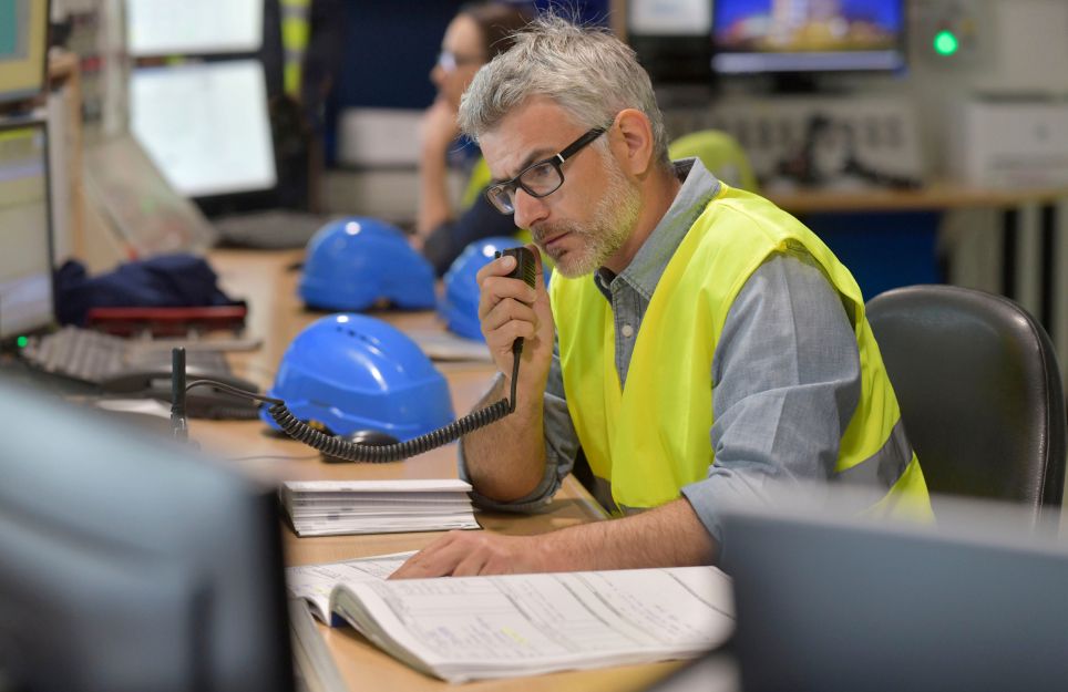 Man seated at desk wearing neon yellow vest using a radio